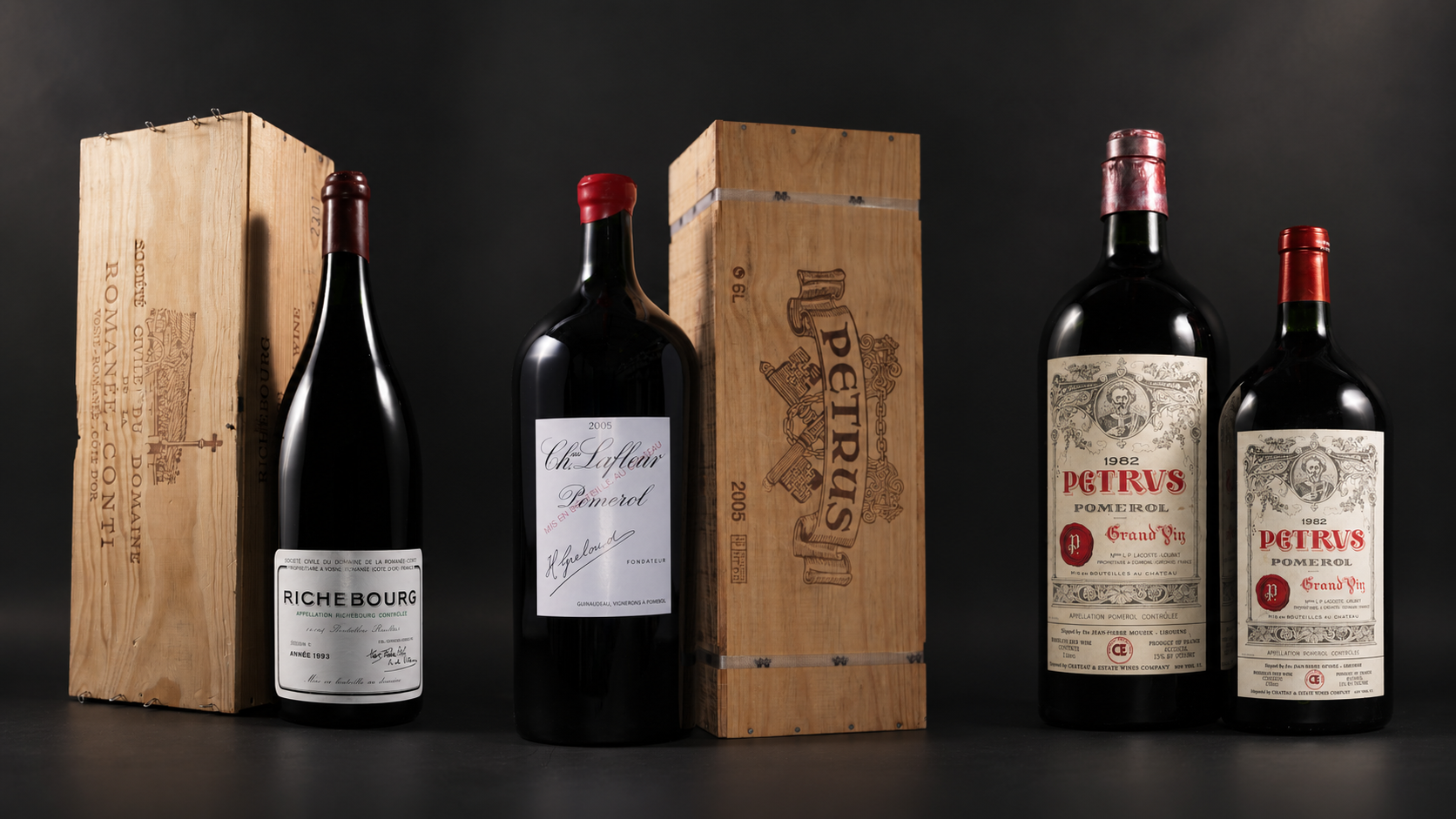 Large-format bottles of Richebourg, Château Lafleur, and Pétrus displayed with original wooden cases against a dark studio background.